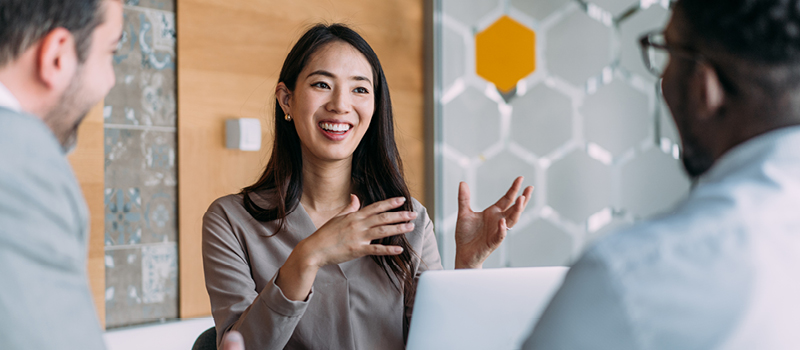 Woman talking animatedly with her two work colleagues in a light, airy office