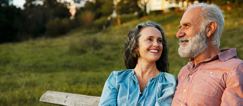 A married couple sitting on a bench outside, smiling.