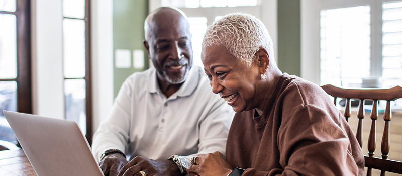 Happy retired couple looking at laptop at kitchen table.