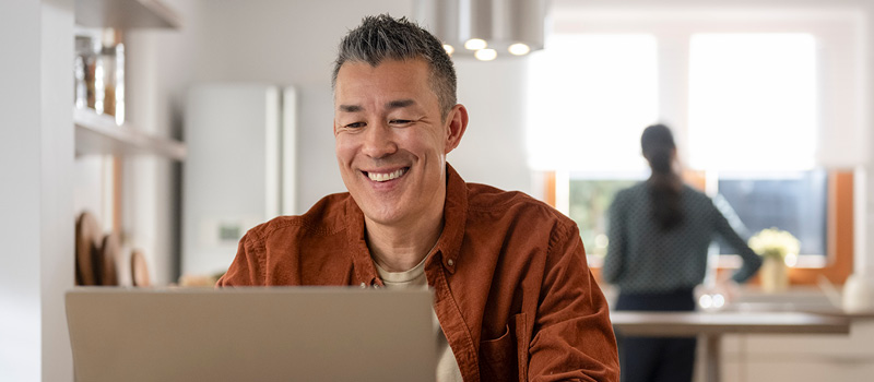 Happy man looking at his laptop, while sitting at the kitchen table.