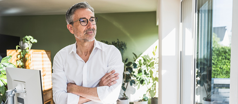 Businessman with arms crossed leaning on desk at home office.
