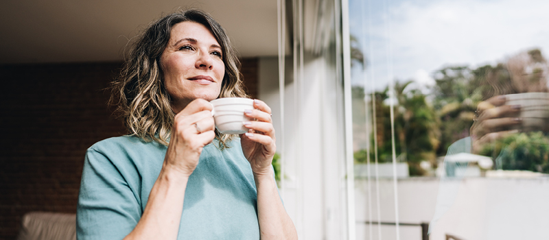 Contemplative mature woman looking through the window at home.
